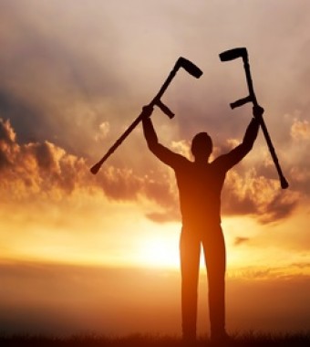 A disabled man raising his crutches at sunset. Medical miracle.